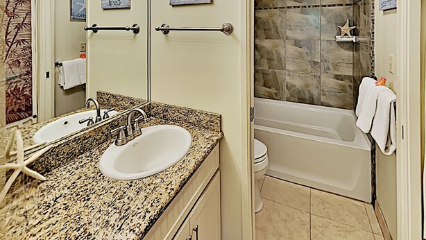 A bathroom with a double sink, a mirror, a shower with a stone wall, and a towel rack. - Maui Banyan T204 1BR condo I Walk to Kamaole Beach (Kihei)