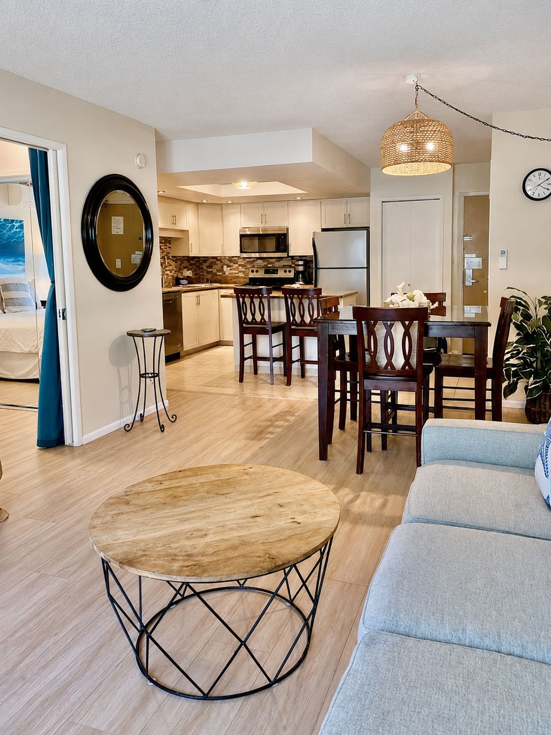 A modern living room with a round wooden coffee table, a grey sofa, and a dining area with wooden chairs.