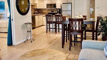 A modern living room with a round wooden coffee table, a grey sofa, and a dining area with wooden chairs.