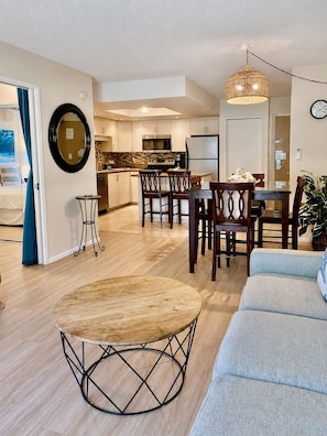 A modern living room with a round wooden coffee table, a grey sofa, and a dining area with wooden chairs.