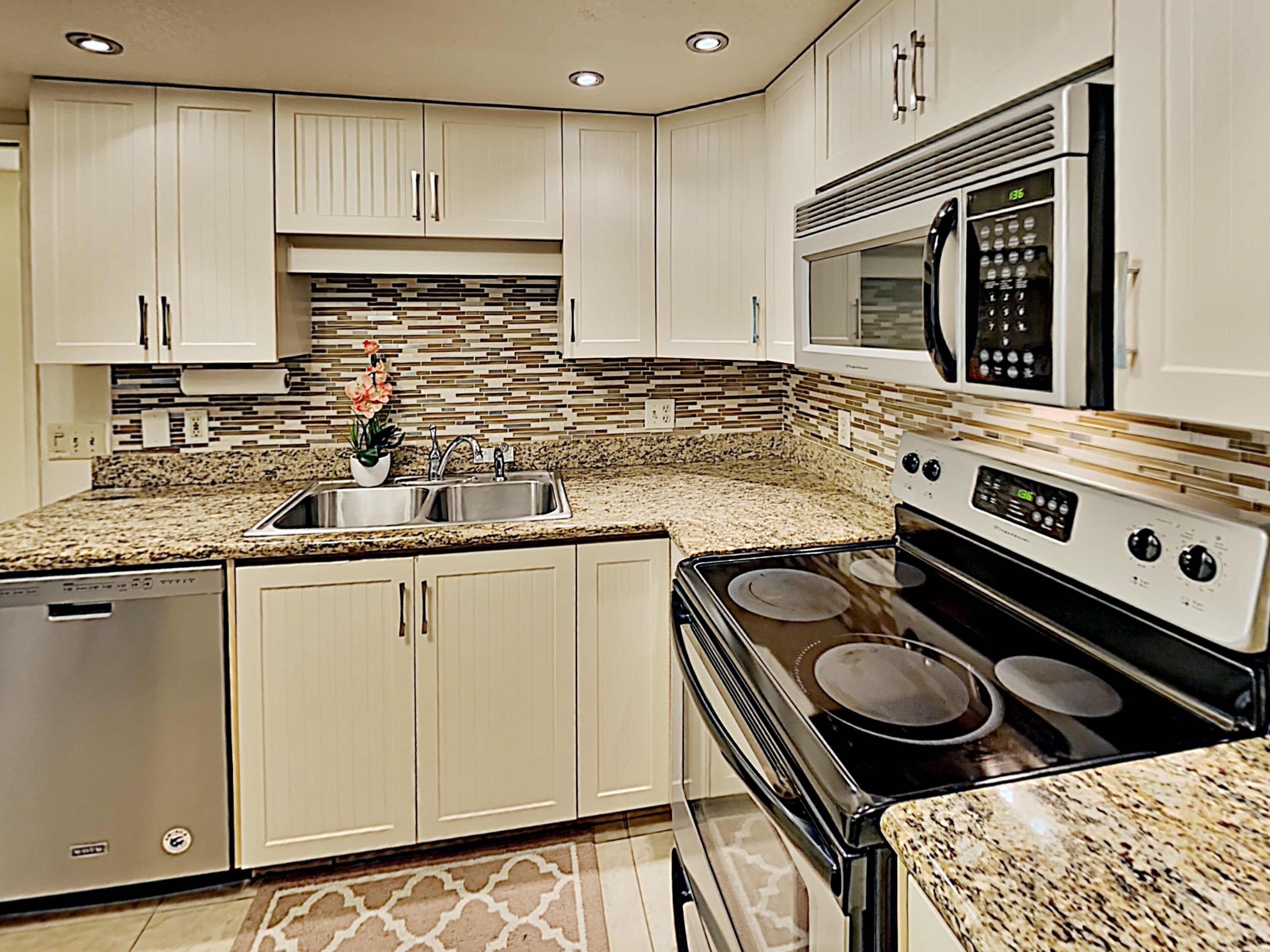 A modern kitchen with white cabinets, a granite countertop, stainless steel appliances, and a backsplash with a mosaic tile pattern.