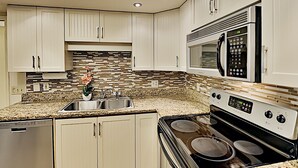 A modern kitchen with white cabinets, a granite countertop, stainless steel appliances, and a backsplash with a mosaic tile pattern. - Maui Banyan T204 1BR condo I Walk to Kamaole Beach (Kihei)