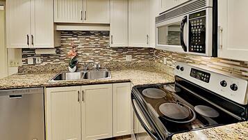 A modern kitchen with white cabinets, a granite countertop, stainless steel appliances, and a backsplash with a mosaic tile pattern.