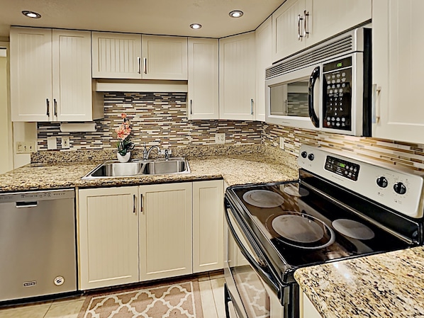 A modern kitchen with white cabinets, a granite countertop, stainless steel appliances, and a backsplash with a mosaic tile pattern.