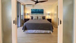 A bedroom with a bed, two bedside tables, a ceiling fan, and a painting on the wall. - Maui Banyan T204 1BR condo I Walk to Kamaole Beach (Kihei)