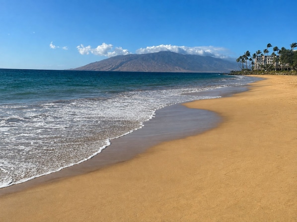 A beach with a mountain in the background, clear skies, and a calm sea. - Maui Banyan T204 1BR condo I Walk to Kamaole Beach (Kihei)