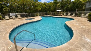 A swimming pool with a curved design, surrounded by lounge chairs and palm trees. - Maui Banyan T204 1BR condo I Walk to Kamaole Beach (Kihei)