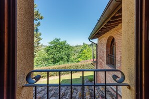 A balcony with a metal railing, a brick building, and a view of a green landscape. - Apartment 'Lucciola' with Shared Pool and Wi-Fi (San Miniato)