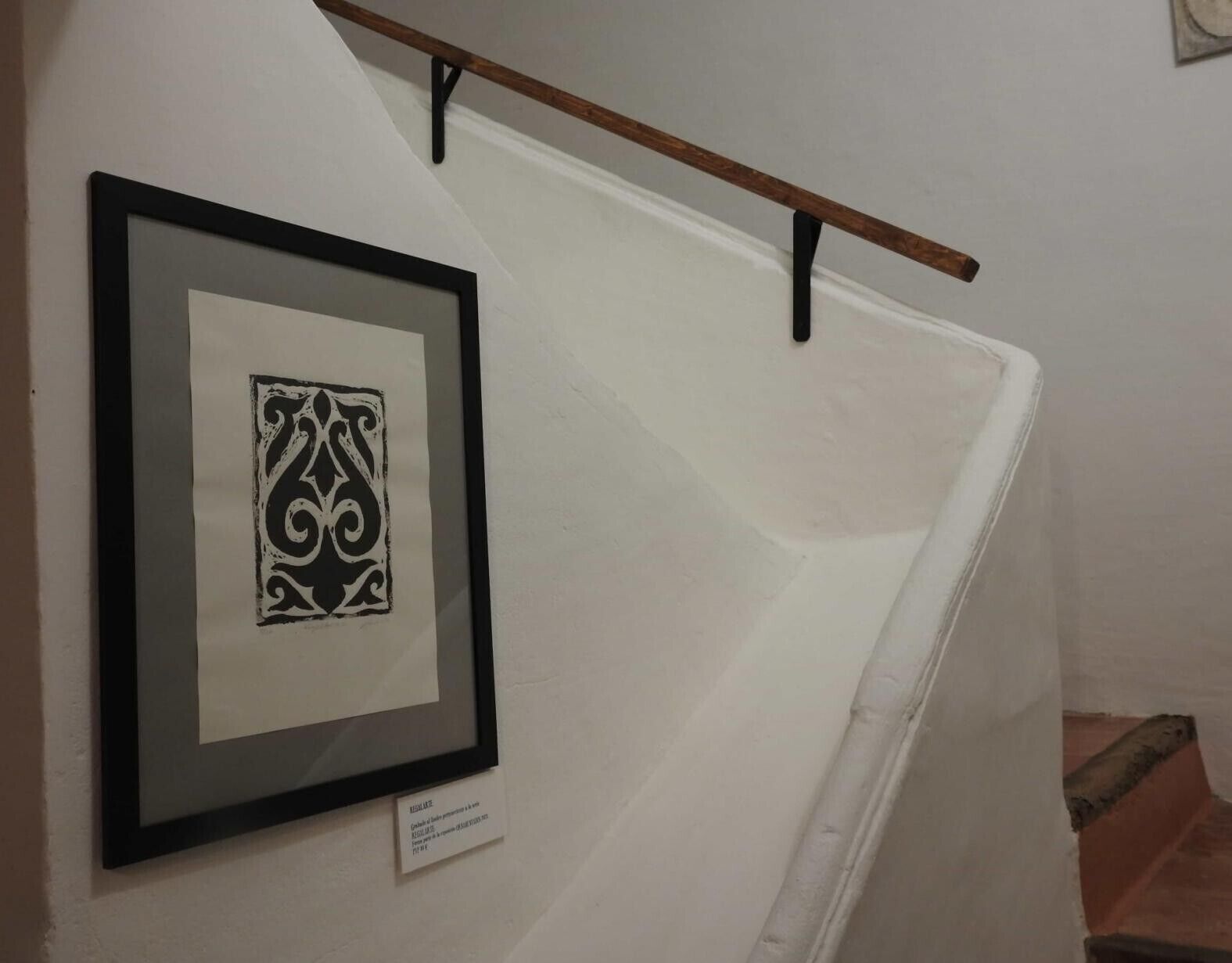 Une œuvre d’art encadrée est accrochée à un mur, et une poutre en bois se trouve au-dessus.