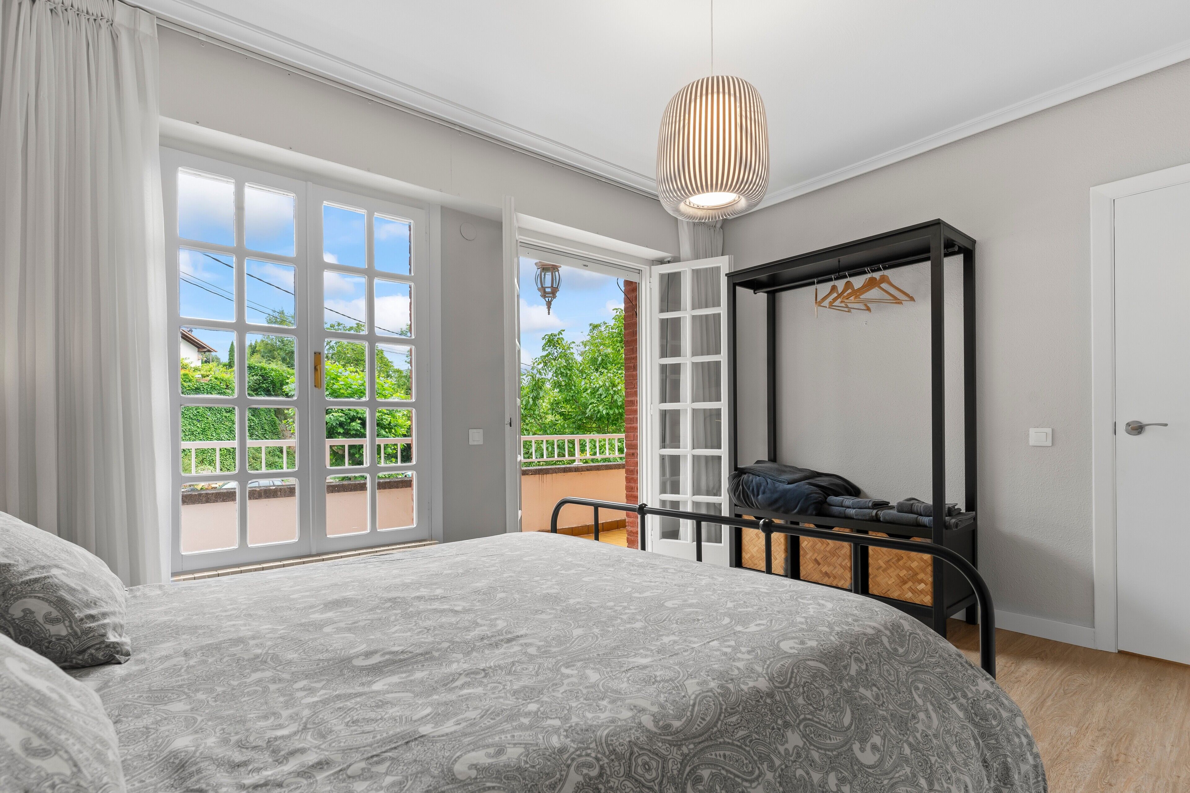 Un dormitorio con cama, armario, perchero y balcón con vistas.