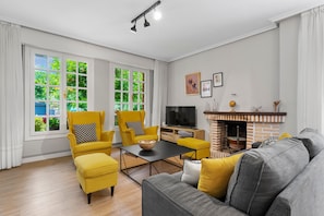 A living room with a fireplace, yellow armchairs, a grey sofa, and a TV. - Casa rural 'Casamentera' con vistas a la montaña, terraza privada y Wi-Fi (Ruesga)