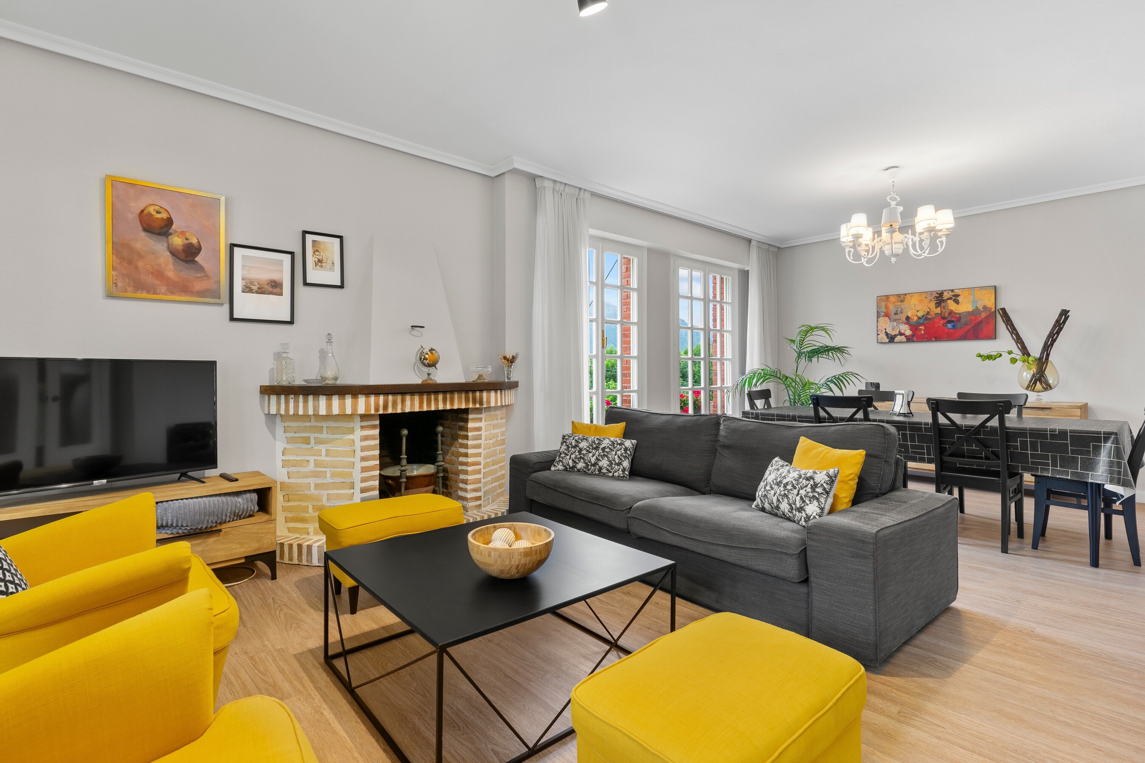 A living room with a sofa, yellow armchairs, a TV, a fireplace, and a dining area with a table and chairs.