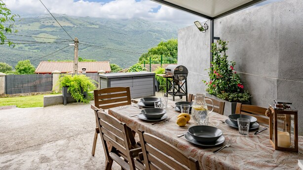 Un espace extérieur aménagé pour les repas, avec une table dressée pour quatre personnes, entourée de chaises, et offrant une vue sur les montagnes en arrière-plan.