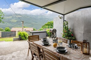 Un espace extérieur aménagé pour les repas, avec une table dressée pour quatre personnes, entourée de chaises, et offrant une vue sur les montagnes en arrière-plan.