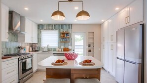 Una cocina moderna con armarios blancos, una isla central, dos lámparas colgantes y un refrigerador de acero inoxidable.