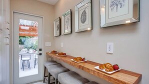 Una cocina con encimera de madera, taburetes de bar, cuadros y vistas a un patio exterior.