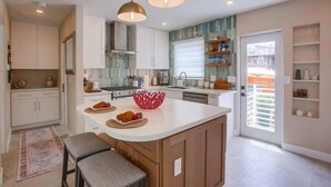 Una cocina moderna con armarios blancos, una isla central, iluminación colgante y vistas al exterior.