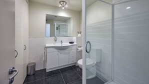 Une salle de bain moderne avec une douche en verre, un lavabo blanc et un grand miroir au-dessus du meuble-lavabo.