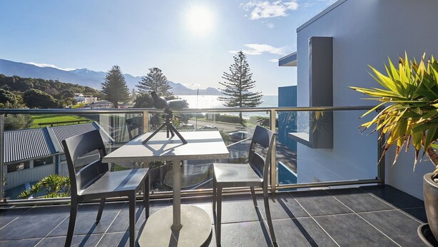 Un balcon avec une table et des chaises, un télescope, et une vue sur des montagnes et une étendue d’eau.