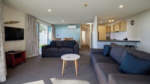 A modern living room with a flat-screen TV, two sofas, a coffee table, and a dining area with a table and chairs. - Kaikoura Luxury Apartments (Kaikoura)
