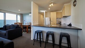 A compact kitchen with a central island, a dining area with a table and chairs, and a living space with a sofa and a coffee table. - Kaikoura Luxury Apartments (Kaikoura)