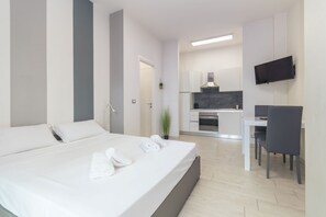 Una habitación de hotel moderna con cama, escritorio, silla, televisor y kitchenette.