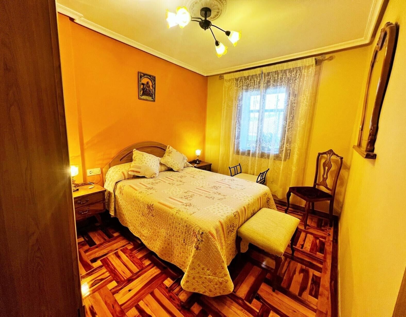A bedroom with a wooden floor, a bed with a patterned bedspread, a chair, a nightstand, and a ceiling fan.