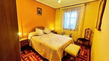 A bedroom with a wooden floor, a bed with a patterned bedspread, a chair, a nightstand, and a ceiling fan.