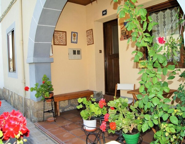 A building with a tiled porch, a bench, a door, and potted plants.