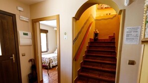 Un couloir avec une porte en bois, une poubelle, un lit dans la pièce adjacente et un escalier muni d’une main courante.