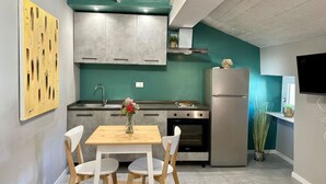 A compact kitchen with a wooden table, two white chairs, a stainless steel refrigerator, and a teal accent wall. - Torino Centro, Romano Suite (Torino)