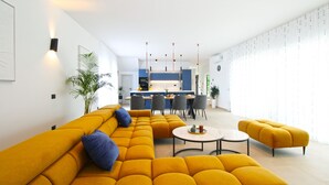 A modern living room with a yellow sofa set, a dining area with chairs, and a kitchen in the background.