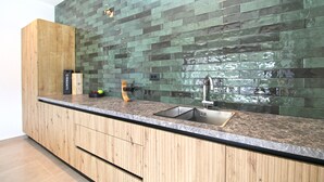 A kitchen with a wooden cabinet, a stainless steel sink, and a green-tiled backsplash.