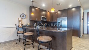 Una cocina moderna con armarios oscuros, una isla central con taburetes de bar, un microondas y un refrigerador.