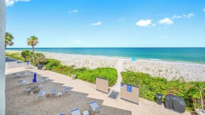 En uteplats vid stranden med solstolar och ett område för grillning, med utsikt över en sandstrand och havet.