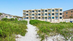 A beachfront hotel with a central walkway leading to a sandy beach area, surrounded by dense greenery. - 🌴BBC 214 - Gulf Front Condo - Pool & Beach are OPEN! (Belleair Beach)