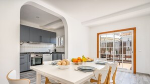 Una cocina moderna con armarios grises, una mesa de comedor blanca con platos y pan, y vista al exterior a través de un ventanal.