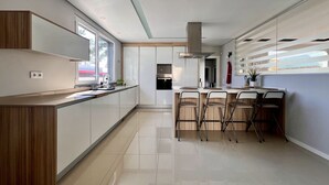 A modern kitchen with a central island, bar stools, and a view of the outside. - Casa Giumeni - House with swimming pool (Fernão Ferro)