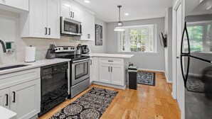 A modern kitchen with white cabinets, stainless steel appliances, and a window providing natural light. - Raleigh Retreat close to NCState, DWNTN and Rex (Raleigh)