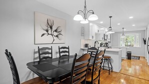 A modern kitchen with white cabinets, a dining table with chairs, and pendant lighting. - Raleigh Retreat close to NCState, DWNTN and Rex (Raleigh)