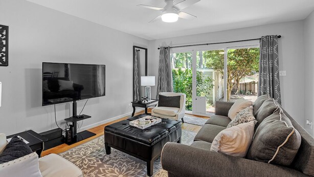 A living room with a flat-screen TV, a ceiling fan, a sofa, a coffee table, and a view of the outdoors. - Raleigh Retreat close to NCState, DWNTN and Rex (Raleigh)