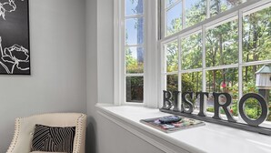 A room with a white cushioned chair, a window with a view of trees, and a sign that reads "BISTRO". - Raleigh Retreat close to NCState, DWNTN and Rex (Raleigh)