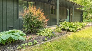 Ein grünes Gebäude mit einer überdachten Veranda, großen Fenstern und einem Garten mit verschiedenen Pflanzen.