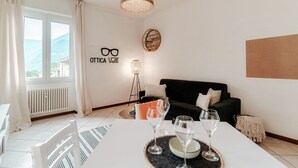 A modern living room with a sofa, a dining table with wine glasses, a floor lamp, and a view of the mountains. - VALLI - MyHomeinComo (Como)
