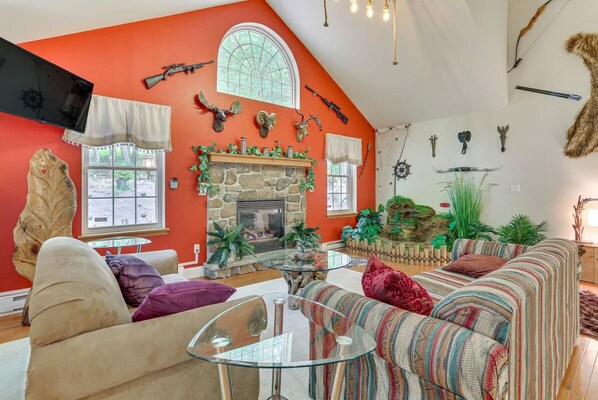 A cozy living room with a stone fireplace, a large window, and a variety of wall-mounted animal heads and weapons.
