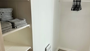 Ein begehbarer Kleiderschrank mit weißen Regalen, einem schwarzen Kleiderständer und Holzboden.