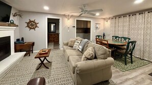 Ein Wohnzimmer mit Kamin, ein Essbereich mit Tisch und Stühlen sowie eine Küche im Hintergrund.
