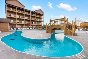 A multi-story building with a pool area, including a wooden bridge and lounge chairs.