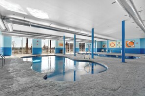 An indoor swimming pool with clear blue walls, a tiled floor, and visible ceiling pipes.