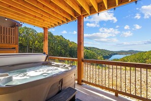 A hot tub on a wooden deck with a view of a lake and forest.
